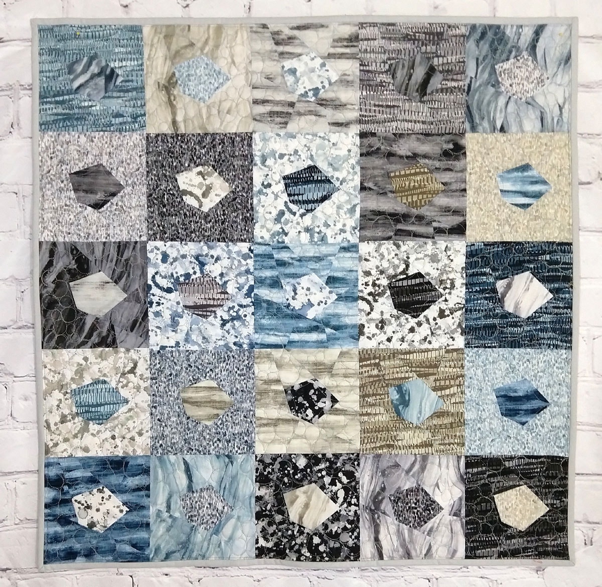 GO Crazy Quilt block pattern with binding on a white brick wall